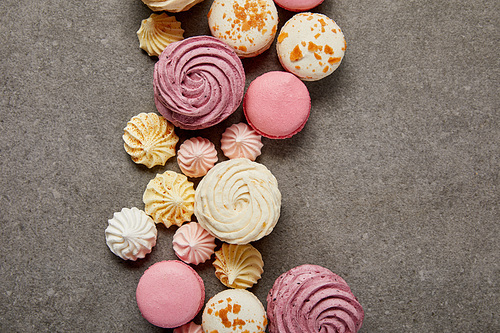 Top view of sweet soft zephyr, small fresh meringues and french macaroons on gray background