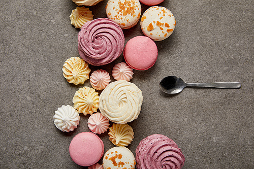 Top view of pink and white macaroons with pink, yellow and white meringues with teaspoon on gray background