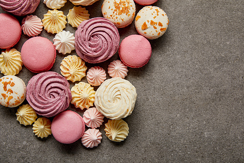 Top view of assorted delicious french macaroons with meringues on gray background
