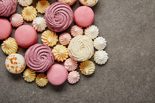 Top view of meringues, macaroons and fluffy white and pink zephyr on gray background