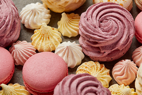 Pink zephyr with small yellow and pink meringues and pink macaroons on gray background