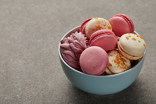 Blue bowl with assorted macaroons and pink zephyr on gray background