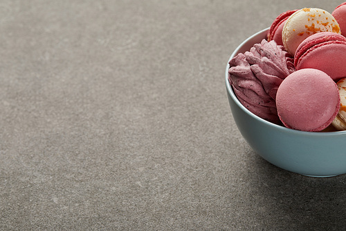 Delicious pink and white macaroons with zephyr in blue bowl on gray background