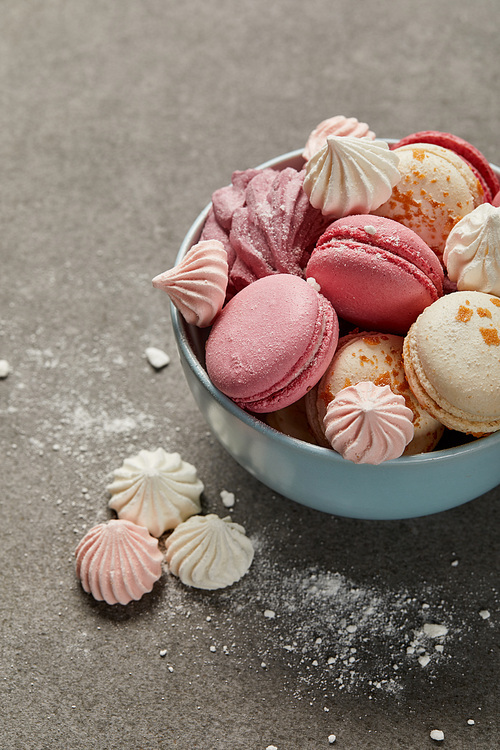 Blue bowl with delicious french macaroons, soft zephyr and small pink and white meringues with crumbs on gray background