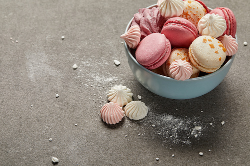 Delicious french macaroons and meringues in blue bowl and smashed sugar pieces on gray background