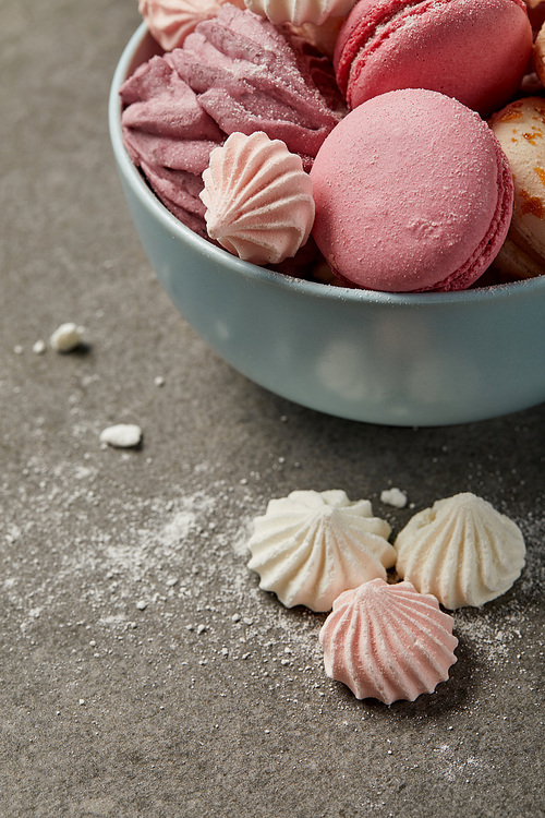 Blue bowl with delicious french macaroons, soft zephyr and small pink and white meringues with sugar pieces on gray background