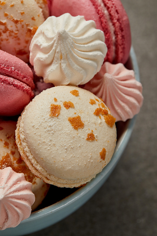 Delicious french macaroons, soft zephyr and small pink and white meringues in blue bowl on gray background