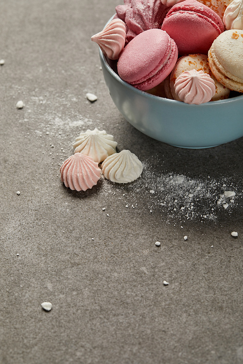 Blue bowl with pink macaroons, soft zephyr and small pink and white meringues with sugar pieces on gray background