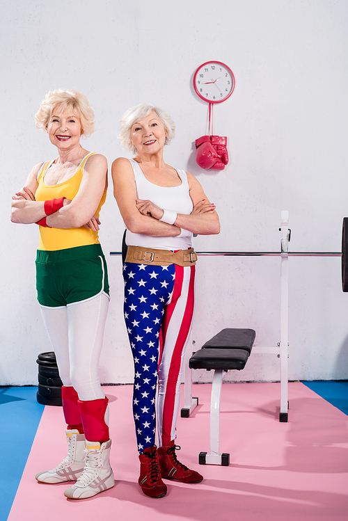 sporty senior women standing with crossed arms and smiling at camera in gym