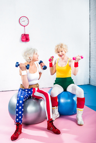smiling senior women in sportswear training with dumbbells and sitting on fitness balls