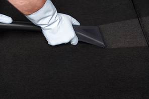 close-up partial view of person in rubber gloves cleaning sofa with vacuum cleaner