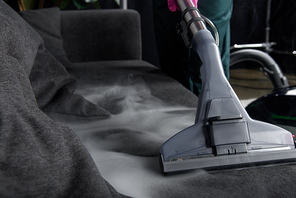 close-up view of person cleaning sofa with vacuum cleaner, hot steam cleaning concept