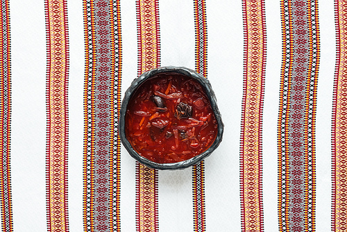 top view of traditional tasty beetroot soup with embroidered towel on background