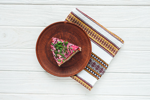 top view of tasty traditional russian salad on plate with embroidered towel on white wooden background
