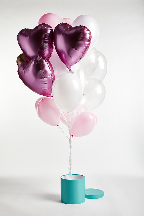 bundle of heart-shaped pink balloons with gift box on white