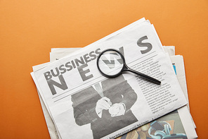 business newspaper near magnifying glass on orange