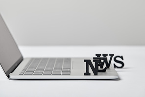 selective focus of news lettering near laptop on grey