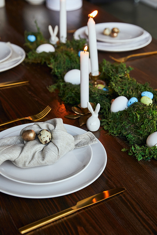 selective focus of quail eggs on napkin and plates near green moss and burning candles on wooden table