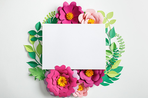 top view of white blank card near paper flowers with green leaves on grey background