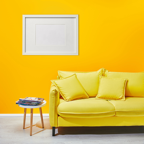 coffee table standing near modern yellow sofa near white frame hanging on wall