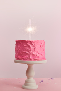 delicious pink birthday cake with sparkler on cake stand isolated on pink