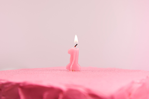 selective focus of burning number one candle on pink and tasty birthday cake isolated on pink