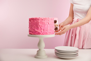 cropped view of woman taking piece of pink birthday cake near white saucers on pink