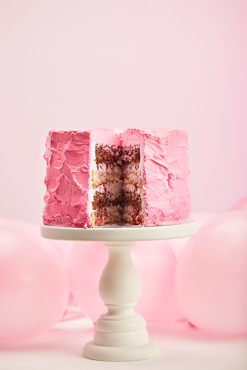 selective focus of tasty cut birthday cake on cake stand near air balloons on pink