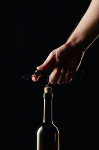 Cropped view of man opening wine bottle with corkscrew isolated on black