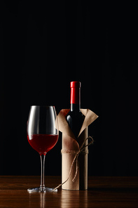 Wine glass and bottle in paper wrapper on wooden surface isolated on black