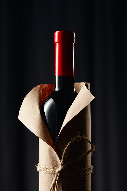 Glass wine bottle in paper wrapper on dark