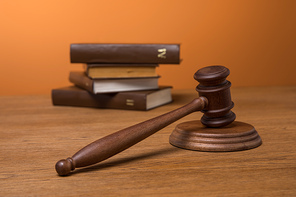 selective focus of volumes of brown books in leather covers and wooden gavel on table on orange background