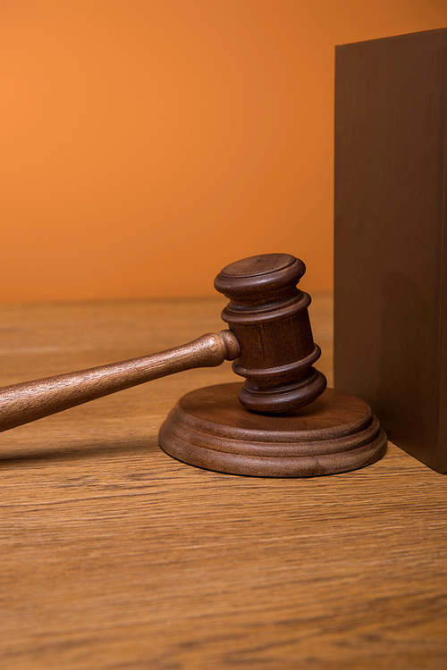 close up of brown book in leather cover and gavel on wooden table isolated on orange