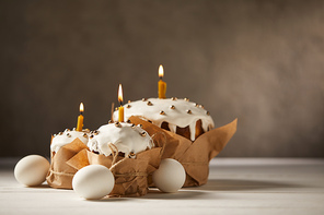 traditional easter cakes with burning candles and chicken eggs on white table with copy space