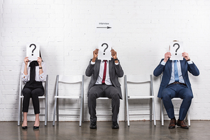 obscured view of multicultural business people holding cards with question marks while waiting for job interview