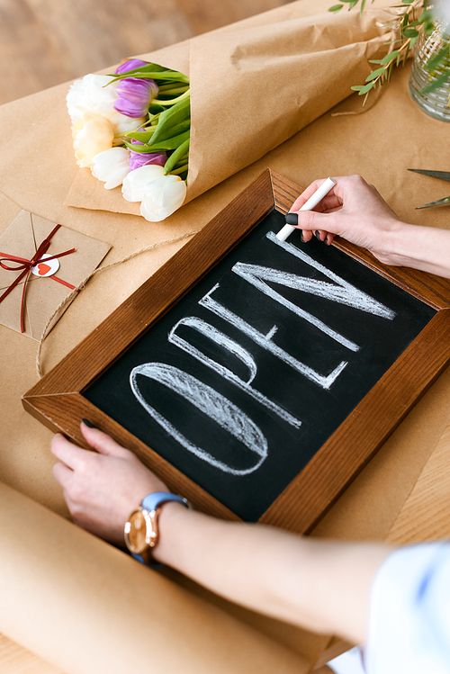 cropped shot of young florist writing word open with chalk on board