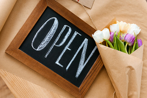 top view of beautiful bouquet of tulips and open sign on craft paper