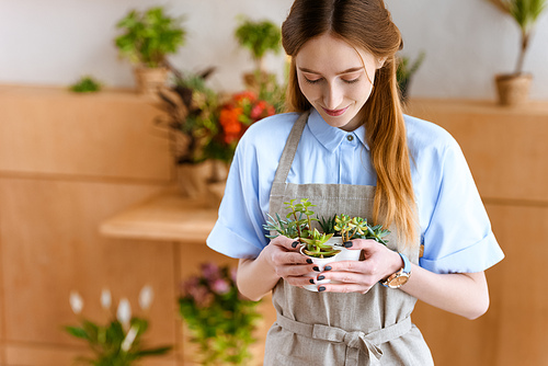 beautiful smiling young florist holding succulents in pots in flower shop