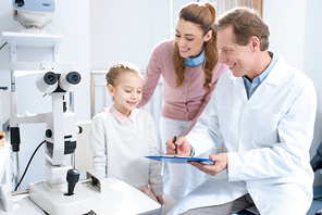 smiling ophthalmologist writing something to patient clipboard in consulting room