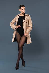 Woman posing in black pantyhose and beige trench on dark background