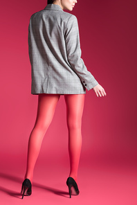 Woman posing in red pantyhose and grey jacket on red background