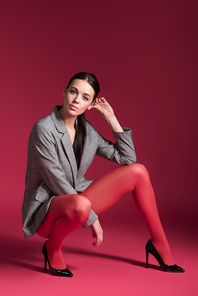 Attractive woman in red pantyhose and grey jacket on red background