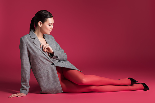 Slim woman in red pantyhose and grey jacket lying on red background