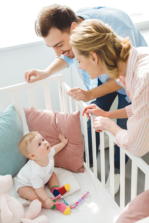 Smiling couple watching infant daughter in crib