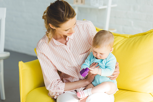 Young mother holding infant daughter with plastic block in hands