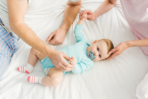 Cropped view of parents playing with baby daughter in bed