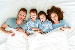 happy redhead family in pajamas lying in bed and smiling at camera