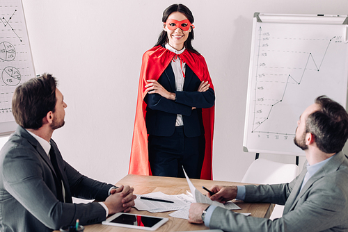 smiling super businesswoman in mask and cape with businessmen in office