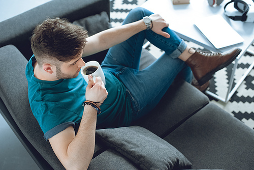 high angle view of young man drinking coffee while sitting on couch