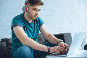 focused young man in headphones using laptop at home